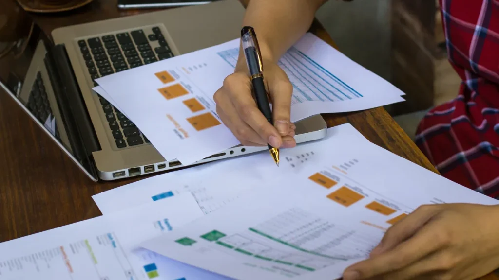 A person reviewing printed financial reports beside a laptop
